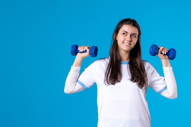 Giovane donna di vista frontale che tiene i manubri blu sulla parete blu