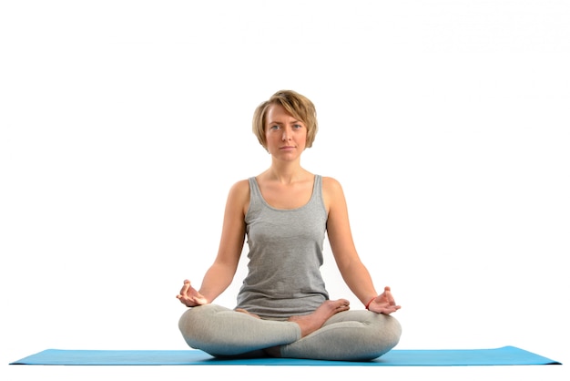 Giovane donna di yoga che medita nella posizione di loto. Isolato sul muro bianco