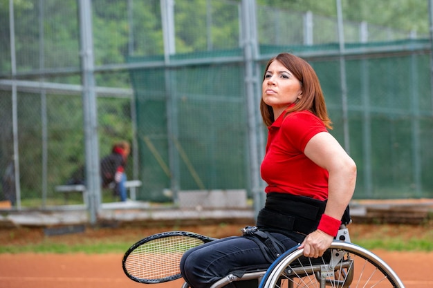 Giovane donna disabile sulla sedia a rotelle che gioca a tennis sul campo da tennis