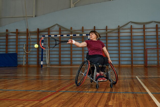 Giovane donna disabile sulla sedia a rotelle che gioca a tennis sul campo da tennis