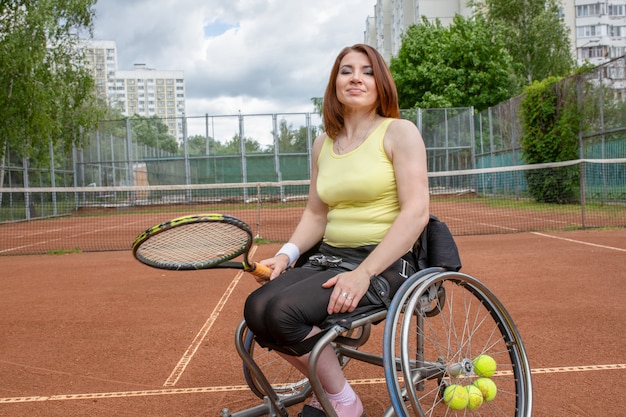 Giovane donna disabile sulla sedia a rotelle che gioca a tennis sul campo da tennis.