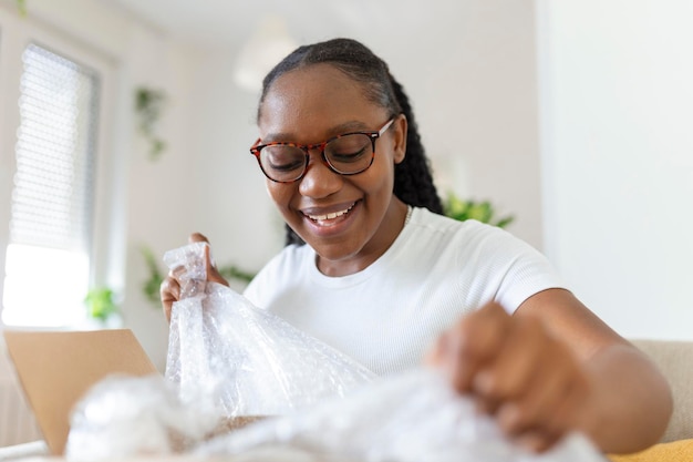Giovane donna disimballa il pacco che ha ordinato online Donna afroamericana è a casa disimballa il pacco consegnato