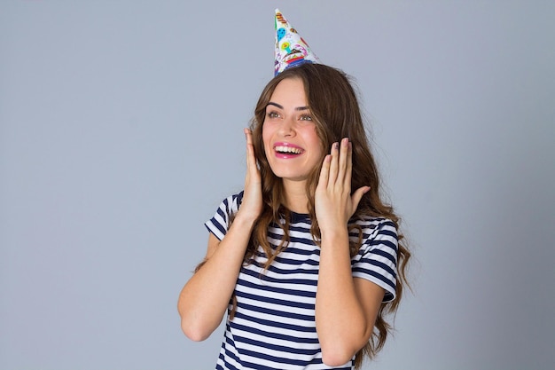 Giovane donna divertita che indossa una maglietta spogliata e un berretto da celebrazione su sfondo grigio in studio