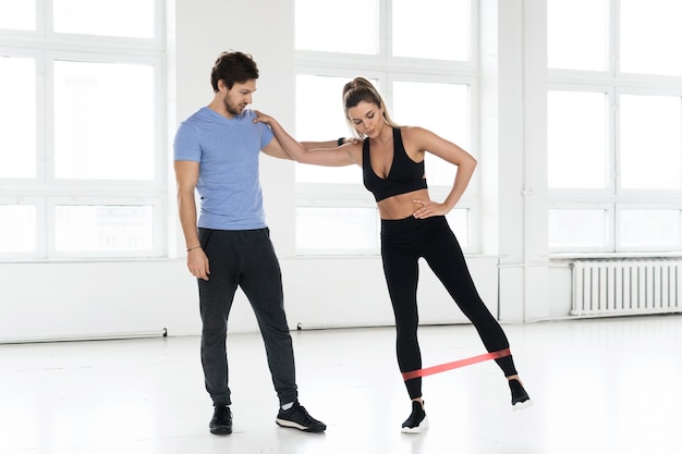 Giovane donna durante l'allenamento con un istruttore di fitness personale utilizzando elastici di resistenza in palestra.