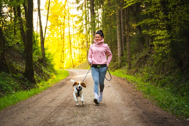 Giovane donna e cane che corrono insieme nella foresta soleggiata