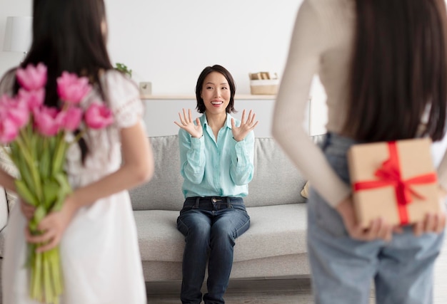 Giovane donna e la sua piccola figlia che tengono fiori e regalo per una donna asiatica senior eccitata dietro