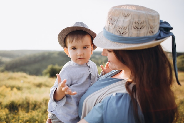 Giovane donna e ragazzino in un campo, all'aperto. Madre che tiene suo figlio, sorridendo, entrambi con abiti vintage e cappelli di paglia.