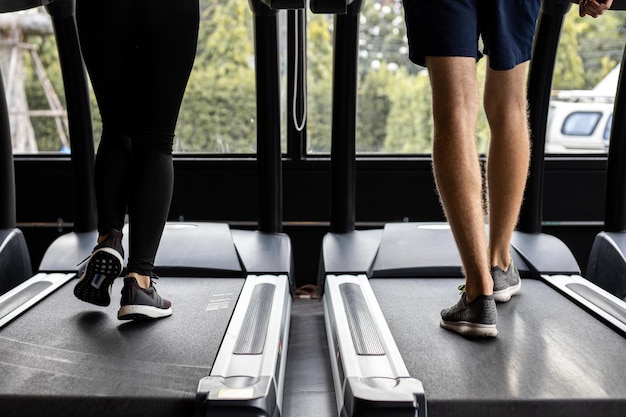 Giovane donna e uomo che corrono fianco a fianco su moderni tapis roulant elettrici in palestra.