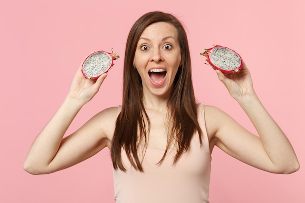 Giovane donna eccitata che tiene la bocca aperta tenendo pitahaya fresco maturo, frutto del drago isolato su sfondo rosa pastello in studio. Lo stile di vita vivido delle persone si rilassa il concetto di vacanza. Mock up spazio di copia.