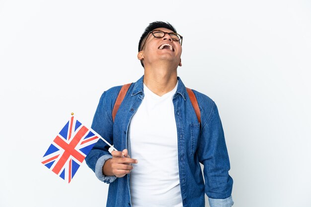Giovane donna ecuadoriana che tiene una bandiera del Regno Unito isolata sul muro bianco ridendo