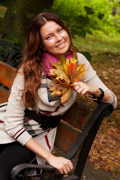 Giovane donna elegante con foglie di autunno seduto sulla panchina