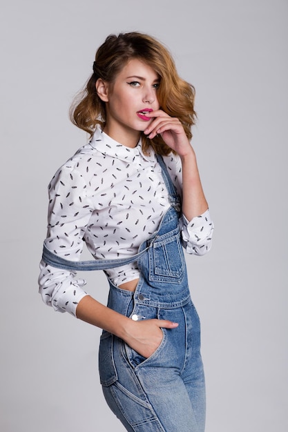 giovane donna elegante in tuta di jeans denim, camicia in posa su sfondo bianco