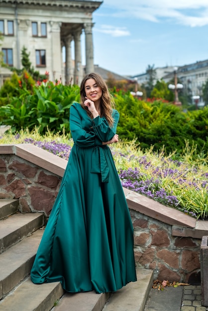 Giovane donna elegante integrale in bello gress verde che sta nella scala di pietra, stile di vita della città