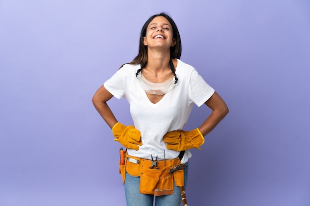 Giovane donna elettricista isolata su viola in posa con le braccia al fianco e sorridente