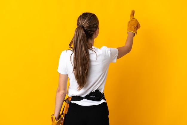 Giovane donna elettricista su giallo che punta indietro con il dito indice