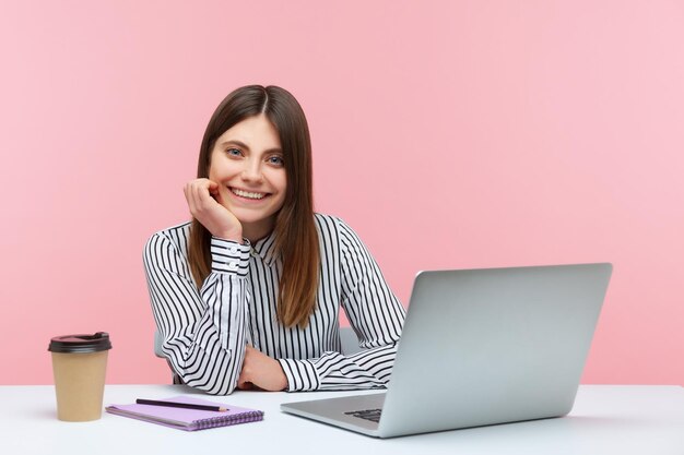 Giovane donna emotiva che si siede e che lavora in ufficio con sfondo rosa