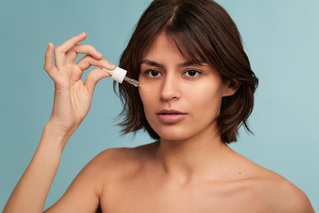 Giovane donna etnica con la pelle perfetta che applica siero sul viso