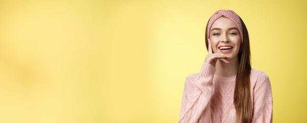 Giovane donna europea attraente intrattenuta allegra in maglione fascia rosa lavorato a maglia che tocca guancia