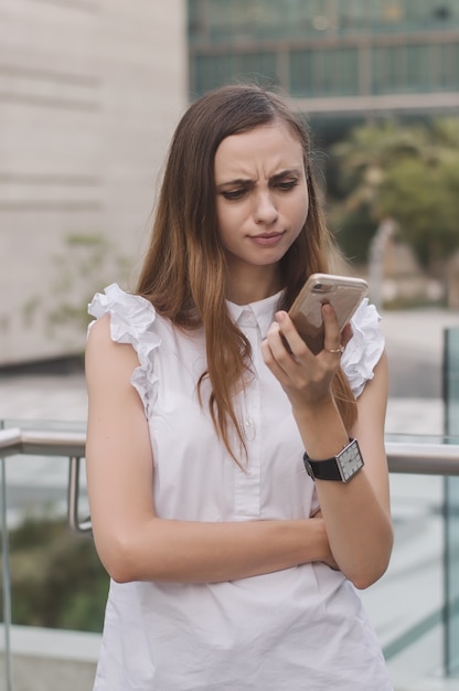 Giovane donna europea guardando il telefono cellulare con l'espressione del viso arrabbiato e stupito