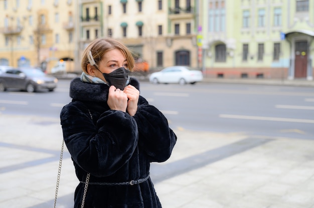 Giovane donna europea in maschera nera medica monouso protettiva in città all'aperto