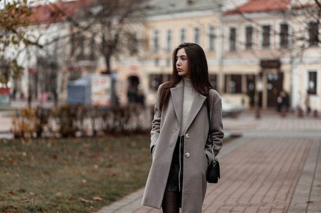 Giovane donna europea in un cappotto grigio alla moda in una strada della città in una giornata autunnale