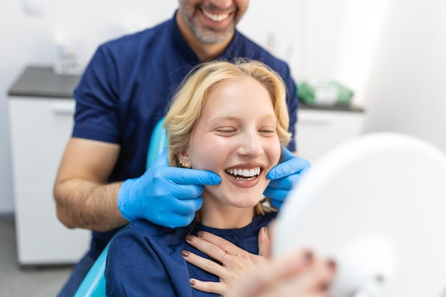 Giovane donna europea sorridente mentre si guarda allo specchio nella clinica odontoiatrica Colpo di una giovane donna che controlla i suoi risultati nell'ufficio del dentista