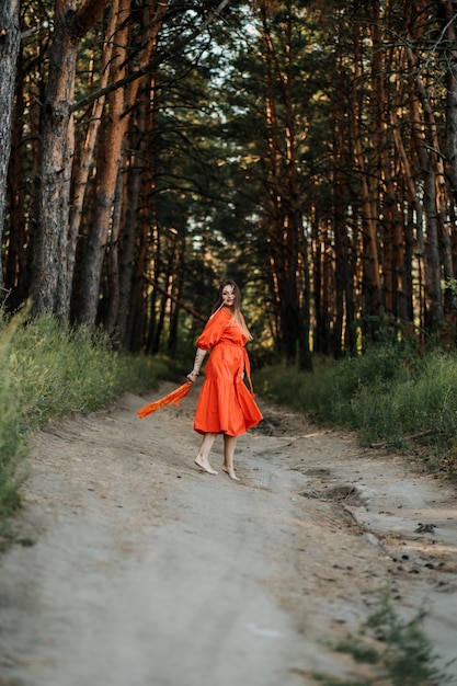 Giovane donna felice a piedi nudi in vestito rosso con la mano alzata che balla nella pineta al giorno d'estate