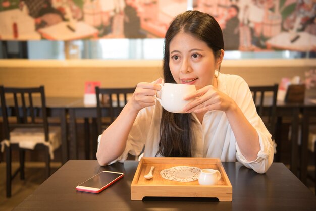 giovane donna felice che beve un delizioso caffè caldo e sogna di pensare alla pianificazione futura seduta nel ristorante caffetteria nel tempo libero in vacanza.