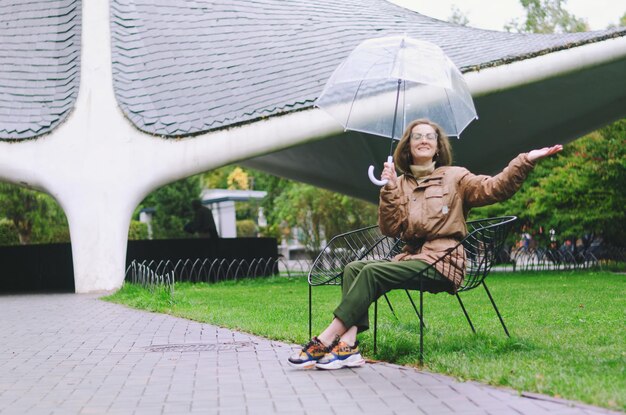 Giovane donna felice che cammina sotto la pioggia nel parco verde con l'ombrello, sorridente, divertente. persona. Tempo di caduta