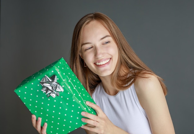 Giovane donna felice che dà una confezione regalo alla fotocamera con un sorriso eccitato che saluta in vacanza e condivide il presente