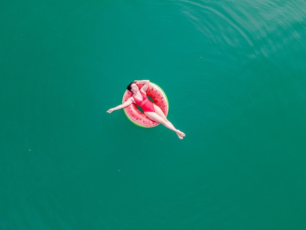 Giovane donna felice che galleggia nell'acqua azzurra blu sulle vacanze estive del cerchio gonfiabile dell'anello