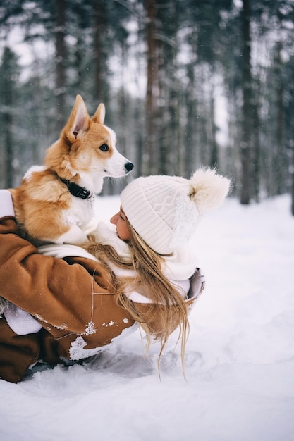 Giovane donna felice che gioca con la sua foresta invernale del cucciolo di welsh corgi pembroke