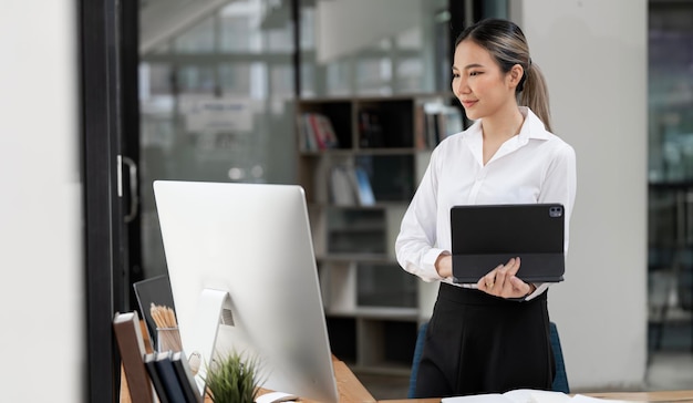 Giovane donna felice che lavora su tablet e computer desktop in ufficio