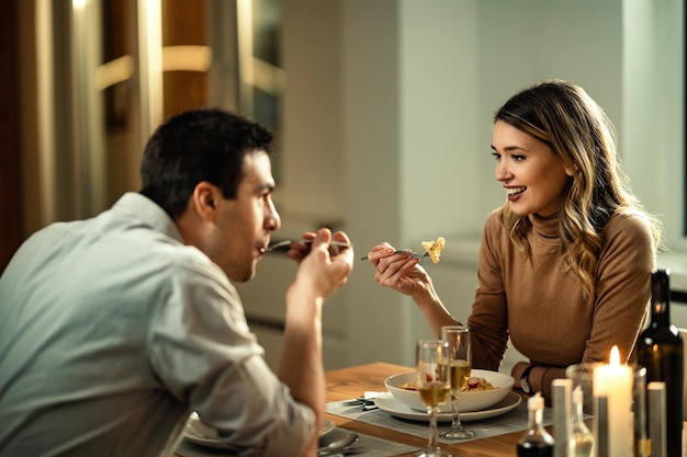 Giovane donna felice che mangia la cena e comunica con il suo ragazzo al tavolo da pranzo