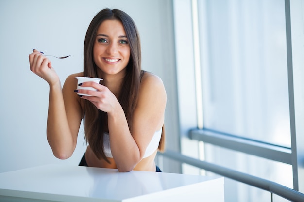 Giovane donna felice che mangia yogurt in cucina