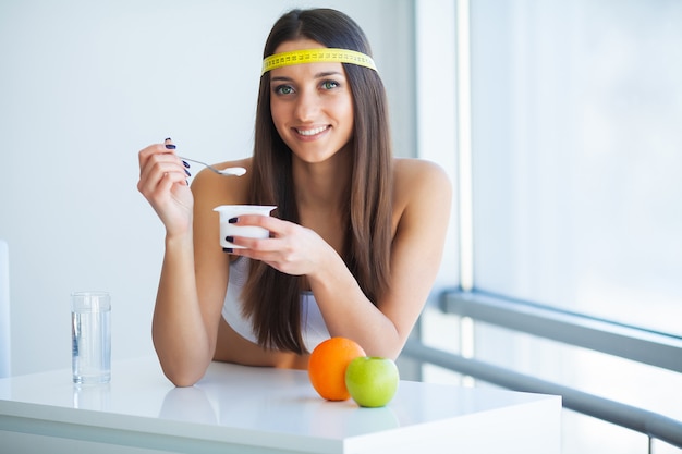 Giovane donna felice che mangia yogurt in cucina