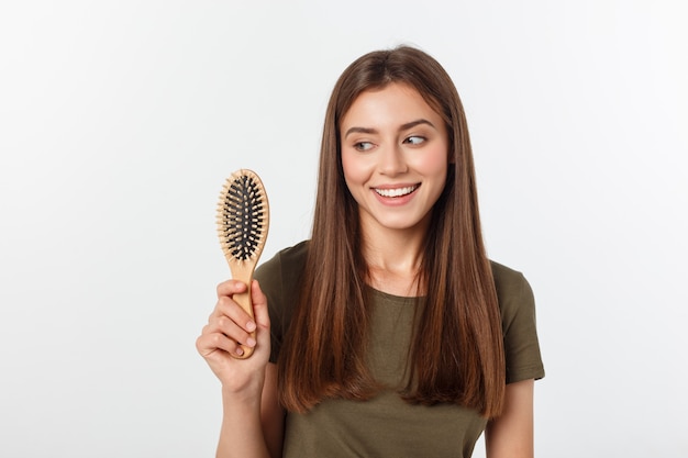 Giovane donna felice che pettina i suoi capelli sani lunghi su fondo bianco.