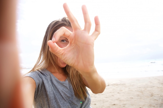 Giovane donna felice che prende la foto del selfie con il segno giusto della mano