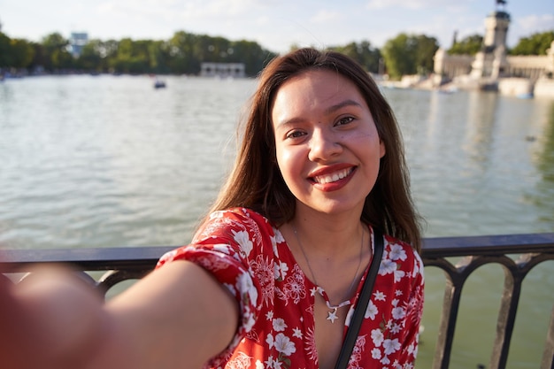 Giovane donna felice che prende un selfie nel lago del parco del retiro a Madrid mentre visita la città