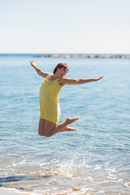 Giovane donna felice che salta sulla spiaggia del mare