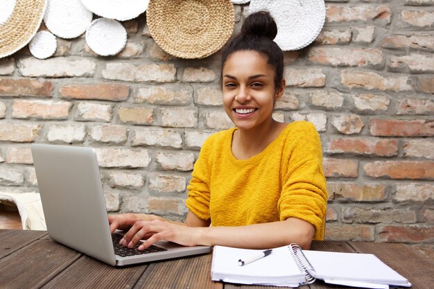 Giovane donna felice che si siede al caffè con il computer portatile