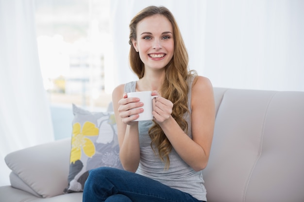 Giovane donna felice che si siede sul sofà che tiene una tazza