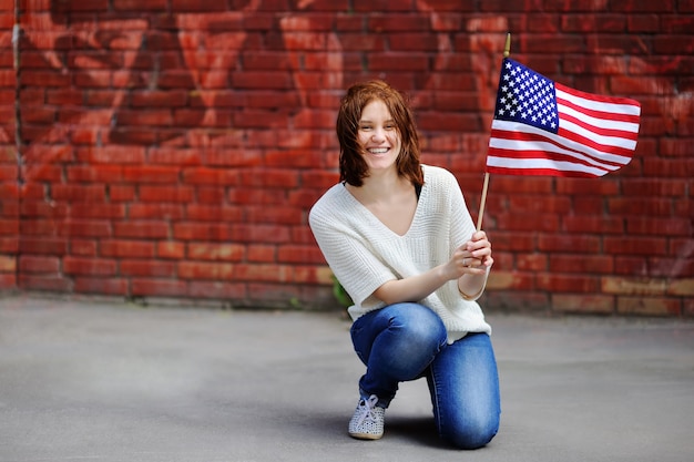Giovane donna felice che tiene bandiera americana. Concetto di Independence Day.