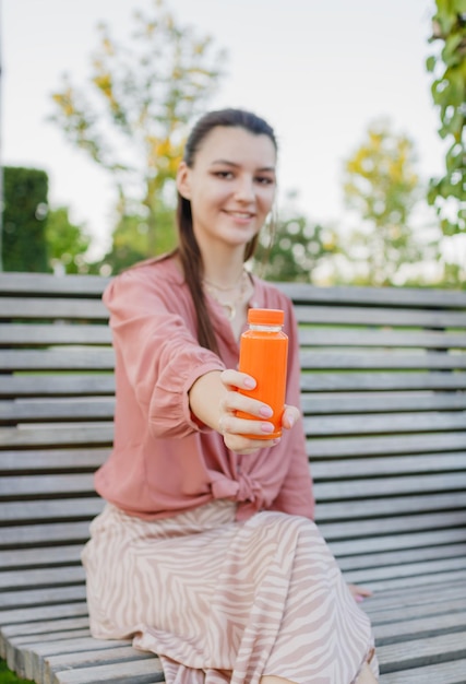 Giovane donna felice che tiene bottiglie con succo d'arancia appena spremuto Giornata estiva all'aperto nel parco