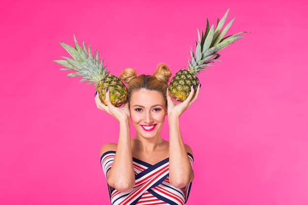 Giovane donna felice che tiene un ananas su una parete rosa.