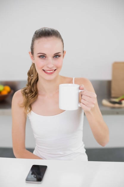 Giovane donna felice che tiene una tazza che guarda l&#39;obbiettivo