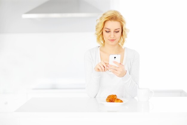giovane donna felice che utilizza lo smartphone in cucina