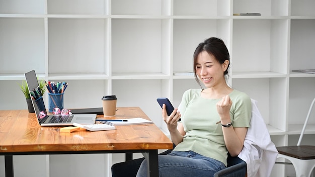 Giovane donna felice che utilizza smartphone e celebra il successo