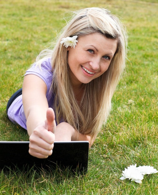 Giovane donna felice che utilizza un computer portatile in un parco