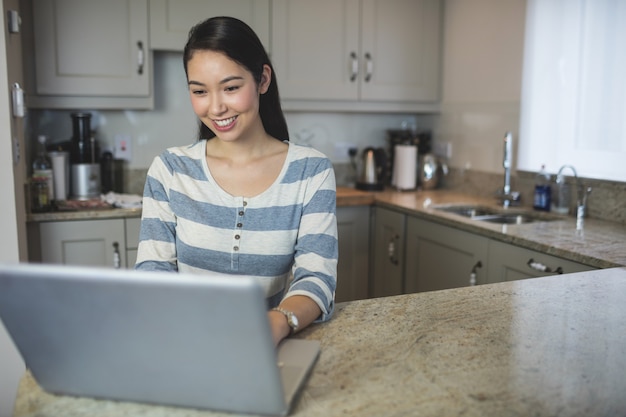 Giovane donna felice che utilizza un computer portatile nella cucina